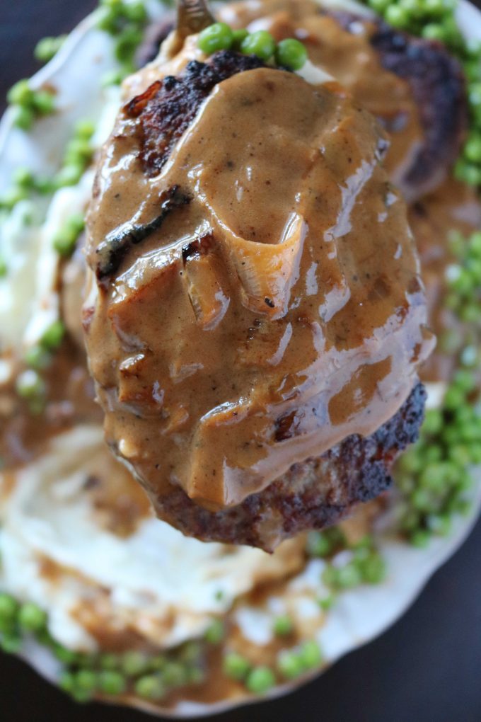 A close up shot of salisbury steak topped with gravy being held over a white serving platter. 