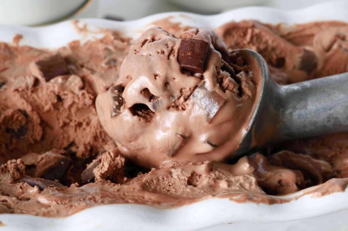 A metal scoop lying in the container of the No Churn Chocolate Ice Cream.