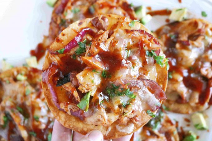 A hand holding a BBQ chicken tostada being held over more tostadas. 