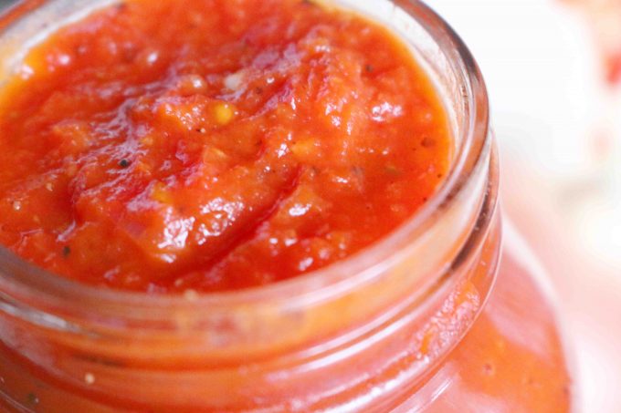 A close up shot of italian marinara sauce in a clear glass jar. 