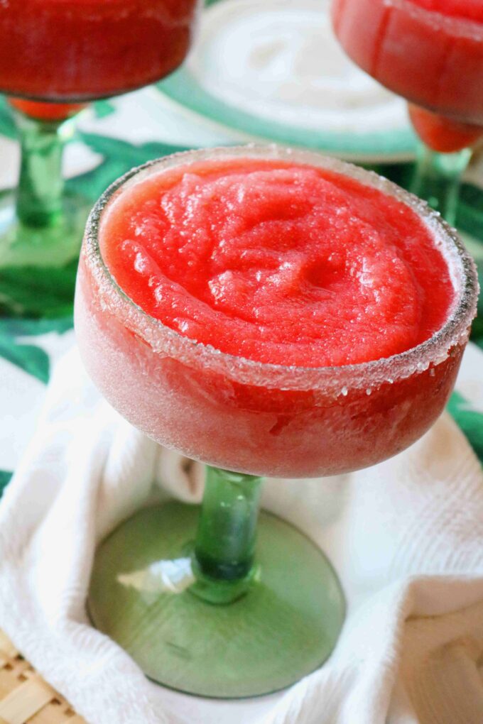 A close up shot of one frozen strawberry margaritas served in a green stemmed margarita glass. 