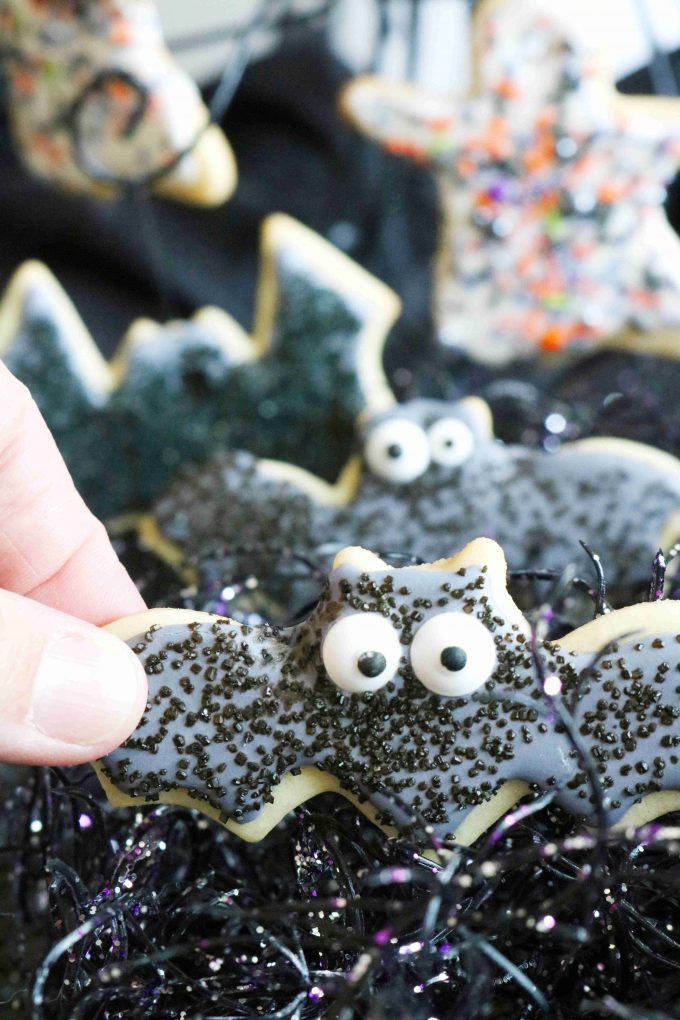 A hand holding a black bat cookie with candy eyes. 