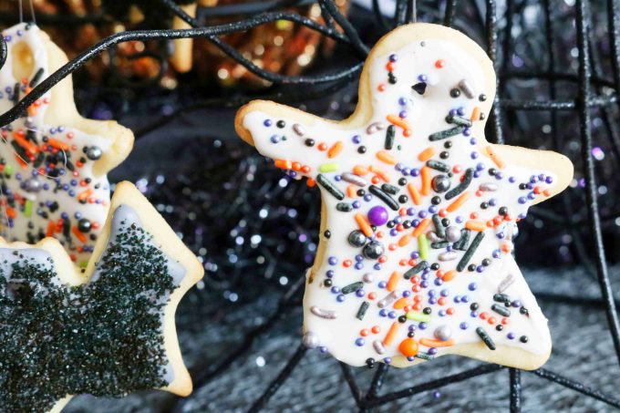 A ghost sugar cookie with white icing and festive halloween sprinkles hanging from fishing line. 