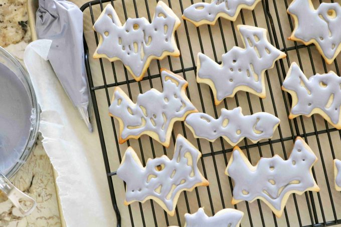 An overhead shot of halloween bat sugar cookies with gray royal icing resting on a black wire rack. 