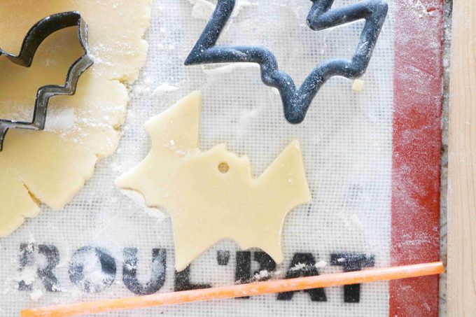 An overhead shot of bat cookie cutters and cookie dough on a silpat. An orange straw is lying at the bottom of the image. 