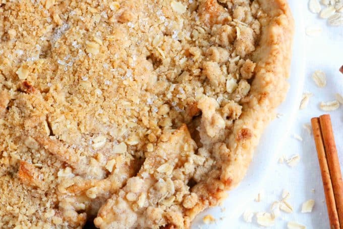 A close up shot of apple crisp pie with one cinnamon stick lying next to the pie. 
