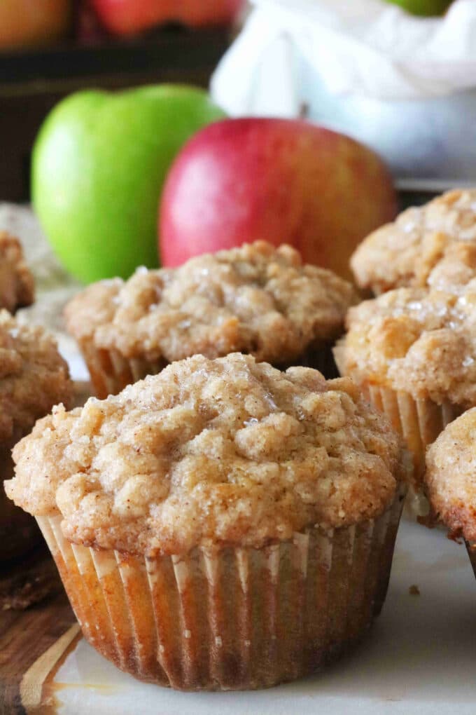 A couple Apple Crumble Muffins with a green and red apple behind them. 