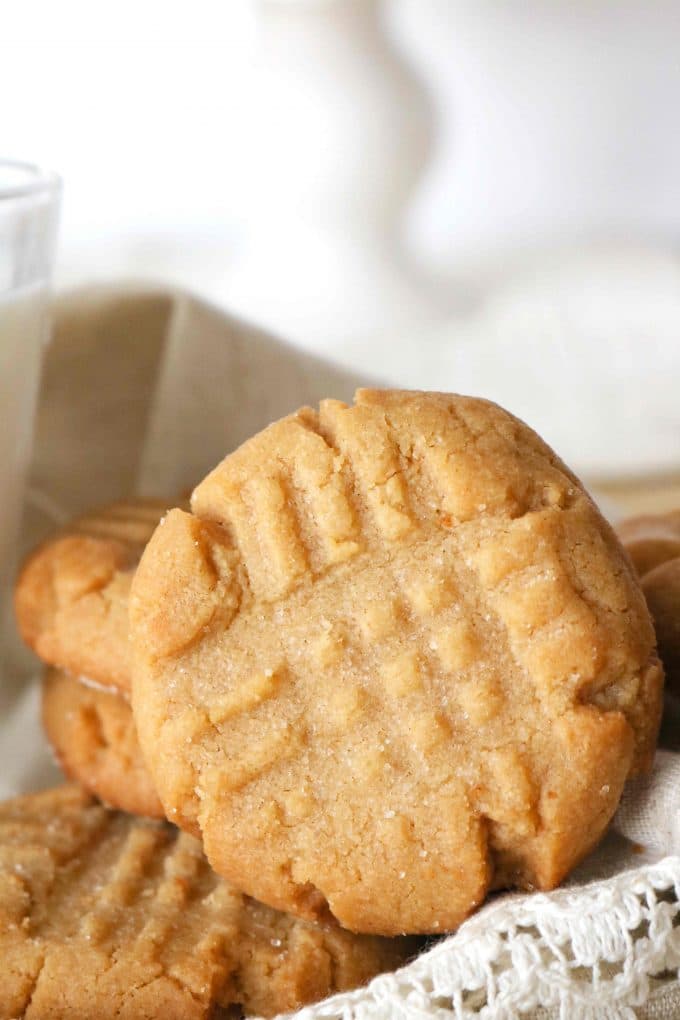 A close up shot of peanut butter cookies served in a basket covered with white linens. 