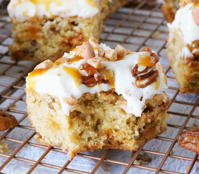 A bite is missing from a square butter pecan blondie that is sitting on top of a wire cooling rack. 