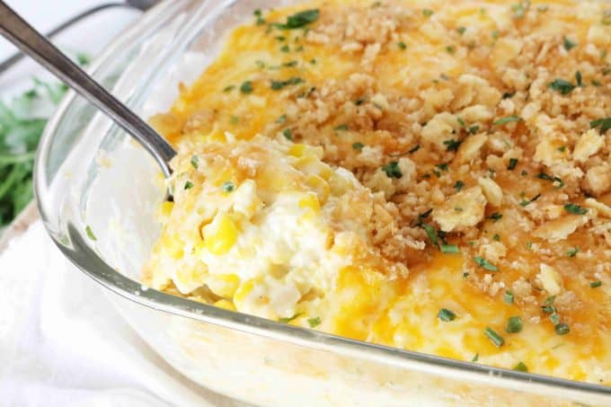 A spoonful of creamy Cream Corn Casserole is being scooped out of a casserole dish.