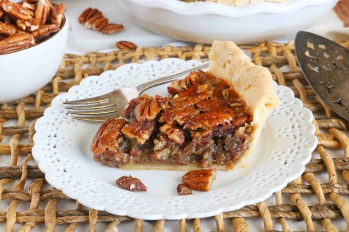 A slice of pecan pie on a white plate. Lying next to the pie is a silver fork. 