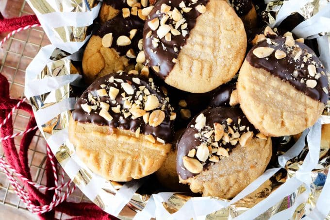 A basket filled with peanut butter cookies with half of the cookie covered in chocolate and peanut pieces. 