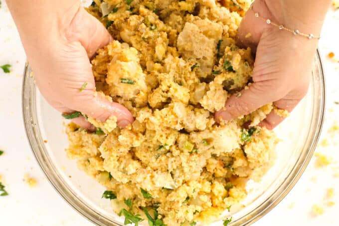 hands mixing the bread, herbs, eggs, broth, and veggies in a bowl