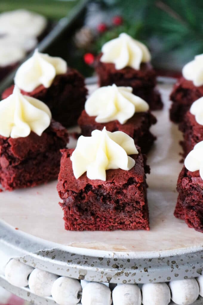 Red velvet brownies squares topped with cream cheese frosting served on a white pedestal stand. 