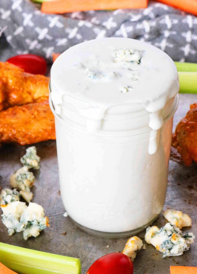 Blue Cheese Dip in a jar surrounded by blue cheese crumbles and buffalo wings.