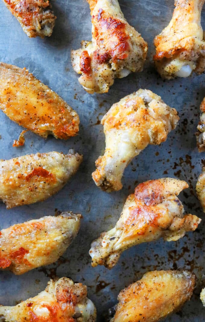 Crispy baked chicken wings with a golden-brown crust spread across a baking sheet.