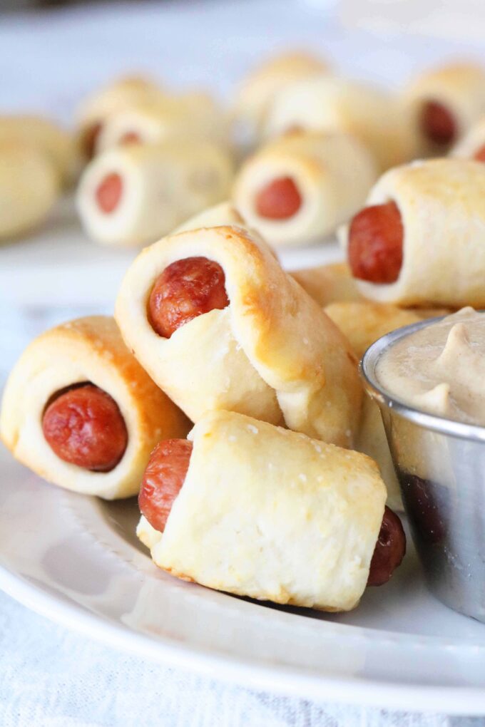 A plate of Pigs In a Blanket with a mustard dipping sauce off to the side.