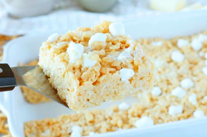 A Peanut Butter Rice Krispie square being held by a spatula over a white casserole dish. 