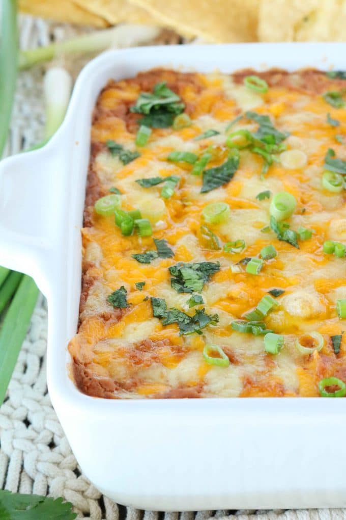 A close up shot of bean dip covered with melted cheese and garnished with green onions in a casserole baking dish.