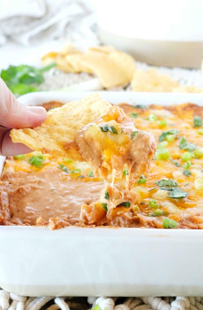 A chip is being dipped into Refried Bean Dip with Cream Cheese.