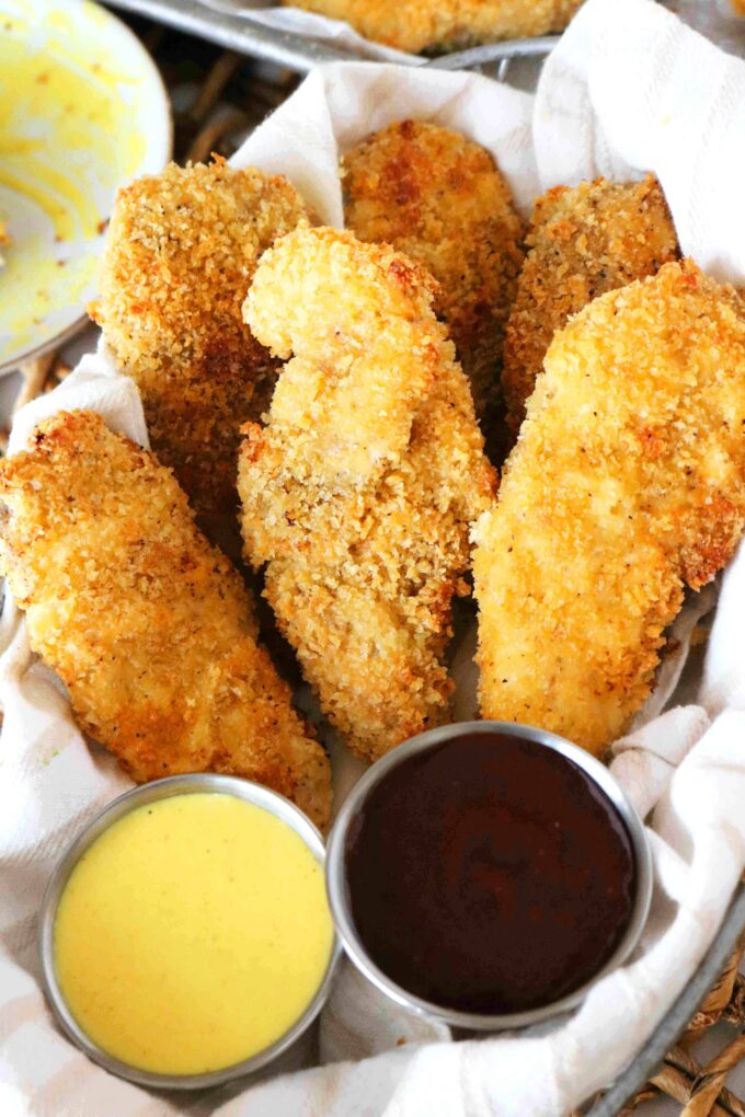 An overhead shot of Baked Chicken Tenderloins in a basket along with two dipping sauces. 