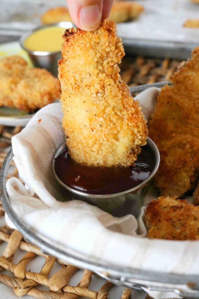A hand dipping one Baked Chicken Tender in a dipping sauce. 
