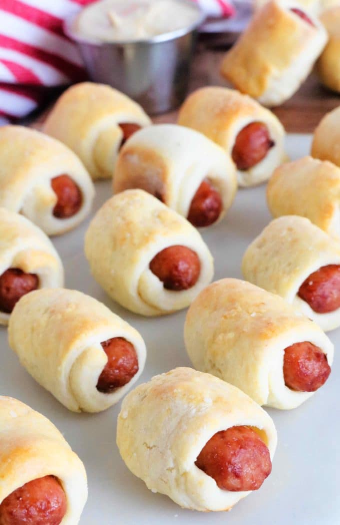 Mini Pigs in a Blanket on a platter with a mustard dipping sauce behind them.