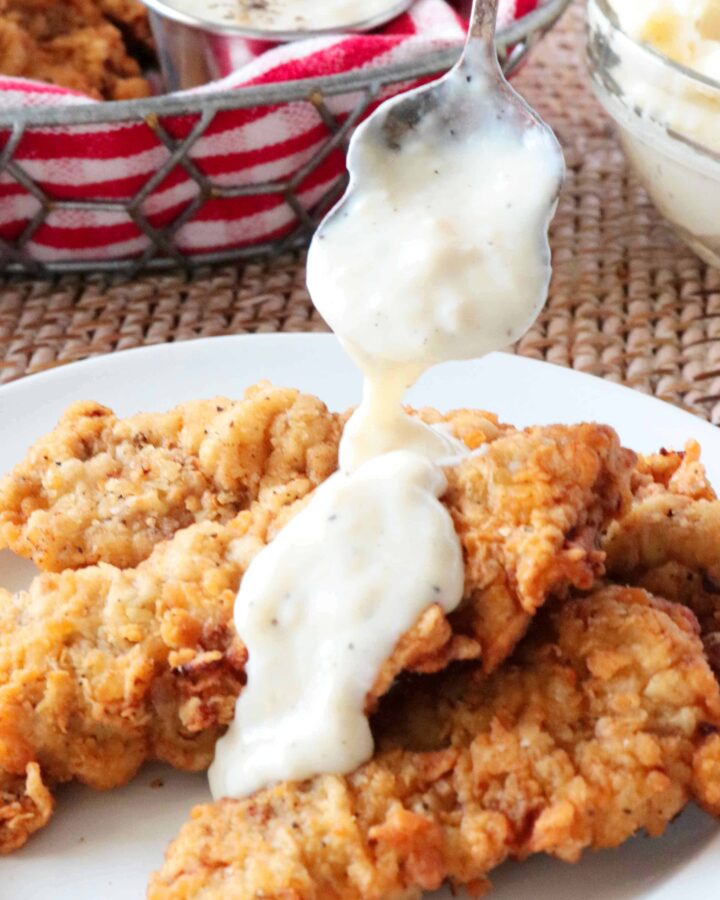 Steak fingers on a plate with a spoonful of country gravy falling over them.