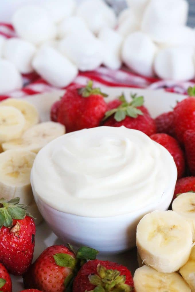 A small bowl of Marshmallow Fruit Dips surrounded by whole strawberries, cut bananas and whole marshmallows. 