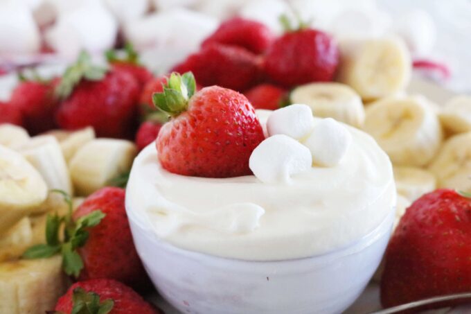 A close up shot of Fruit Dip with Marshmallows and Strawberry. A whole strawberry and three marshmallows are sitting on top of the dip. 