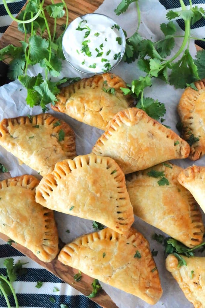 An overhead shot of Mexican Empanadas surrounded by sprigs of fresh cilantro and a small bowl of sour cream. 