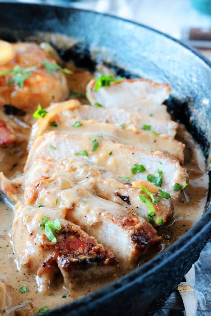 A close up of sliced Smothered Pork Chops cooked in a cast iron skillet. 