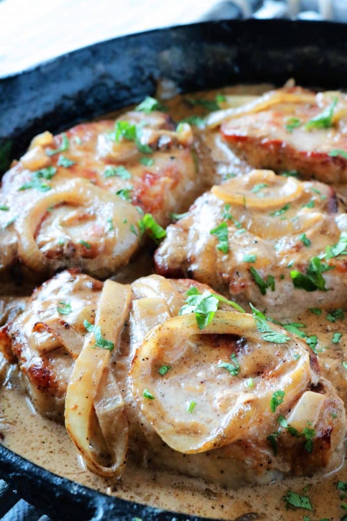 A close up shot of Smothered Pork Chops being cooked in a cast iron skillet. 
