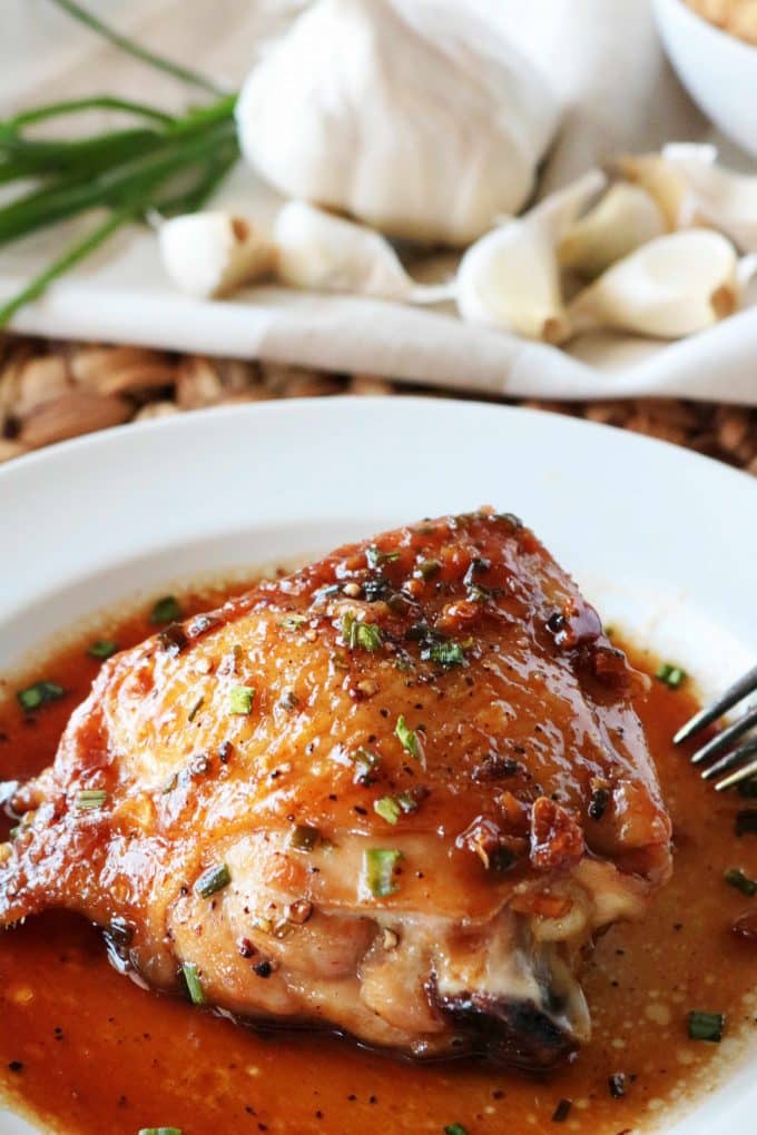 A Brown Sugar Garlic Chicken thigh served on a white plate with garlic cloves in the background. 
