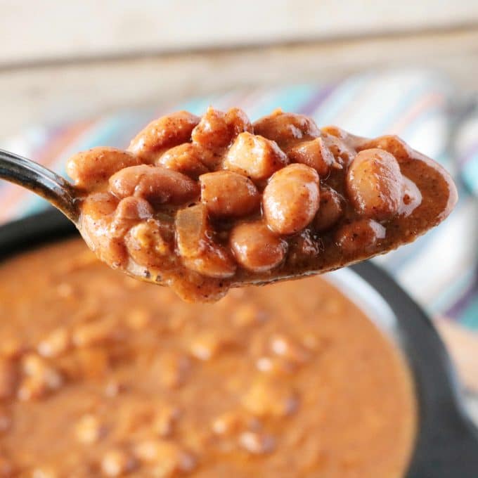 A spoonful of Crock Pot Beans being held over a bowl of the beans. 