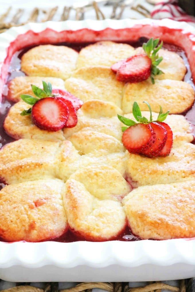 Strawberry Cobbler that has been baked in a white scalloped baking dish and topped with sliced fresh strawberries. 