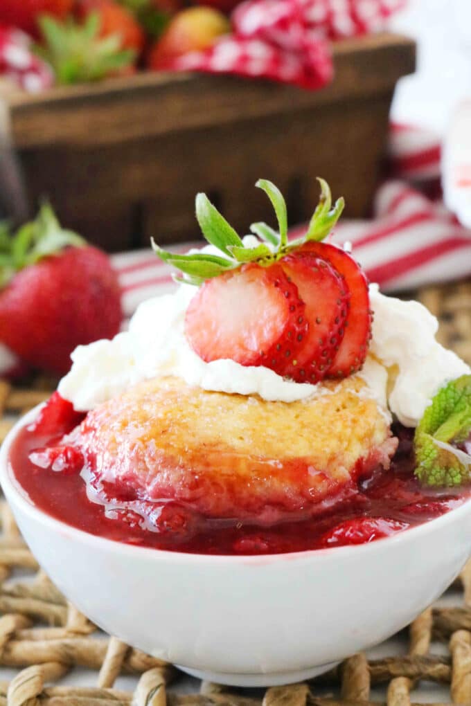 Strawberry Cobbler served in a white bowl topped with a fresh strawberry and whipped cream. 