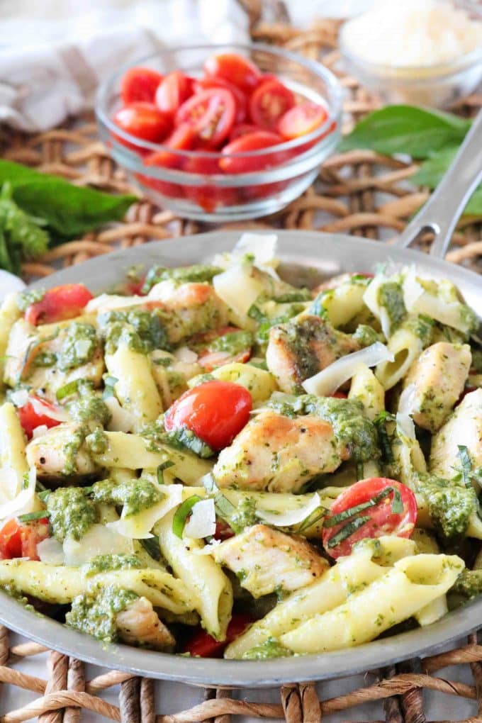 Chicken Pesto Pasta in a saucepan with a clear glass bowl in the background with fresh tomatoes. 