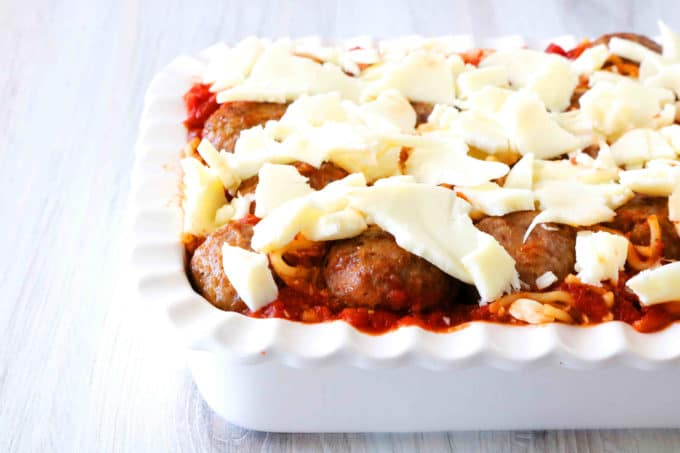 A side view of a white casserole dish filled with meatball casserole before it is cooked. 