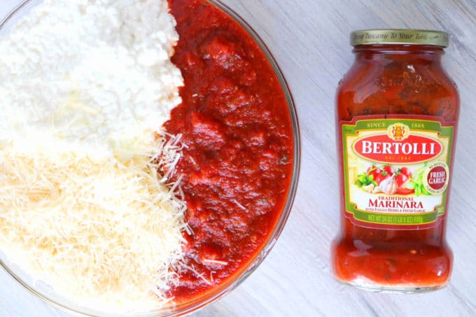 An overhead shot of a bowl with marinara sauce, parmesan cheese and cottage cheese. Lying next to the bowl is a jar of marinara sauce. 