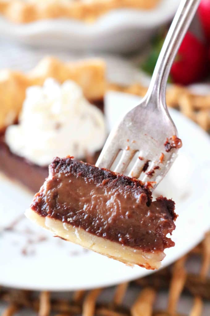 A bite of Chocolate Chess Pie on a fork being held in front of a slice of pie. 