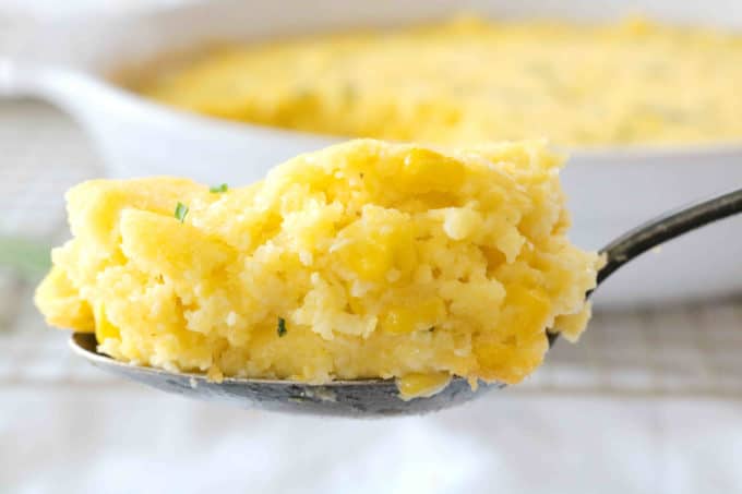 A spoonful of Corn Souffle held in front of a white dish. 