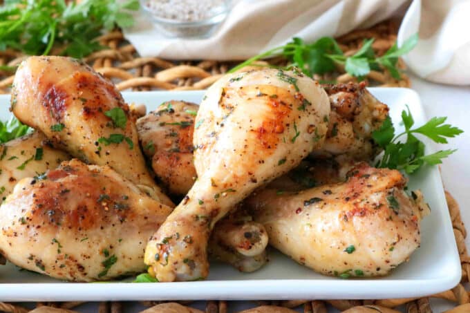 Baked chicken legs stacked on a white platter surrounded by parsley.