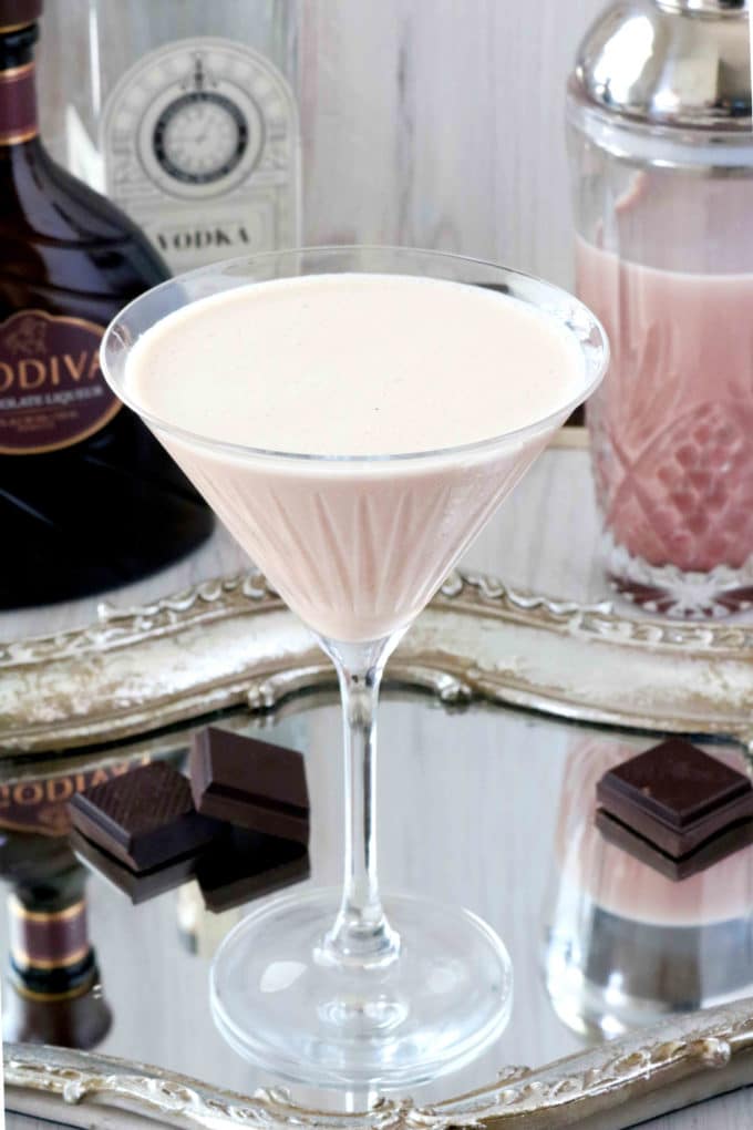 A closeup shot of a chocolate martini in a martini glass surrounded by pieces of chocolate.