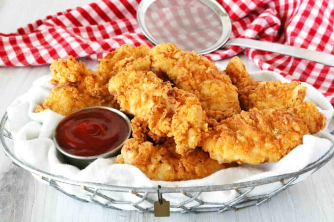 A basket of fried chicken tenders with ketchup for dipping.