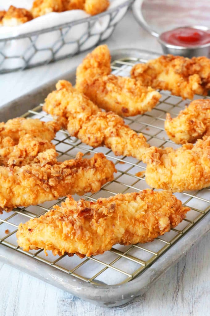Fried chicken strips on a cooling rack situated over rimmed baking sheet.