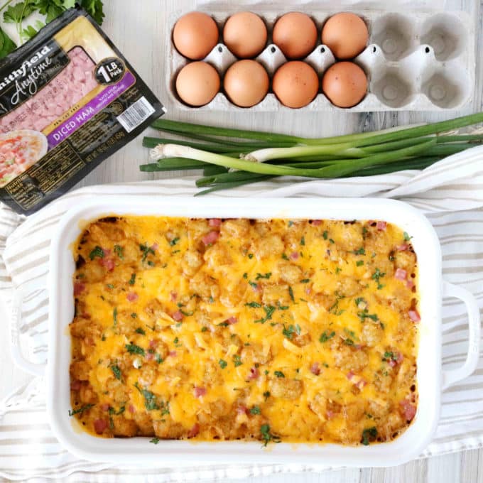 An overhead shot of tater tot breakfast casserole with diced ham, eggs, and green onions laying off to the side.