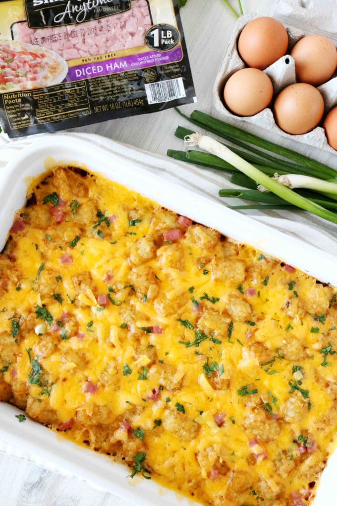 An overhead shot of breakfast casserole with eggs, ham, and green onions off to the side.