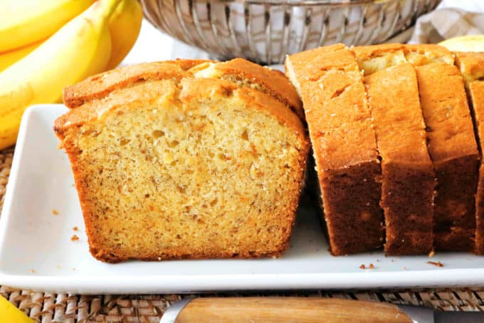 A loaf of banana bread with sour cream, sliced and sitting on a platter.