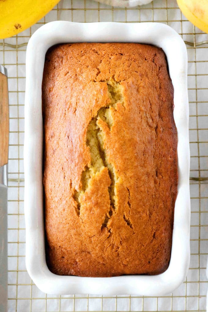 An overhead shot of banana bread with sour cream in a pan on a wire rack with a knife next to it.